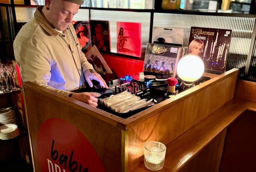 A DJ flicking through a crate of vinyl records and playing music at Baby Driver bar.