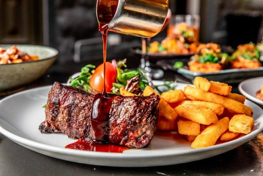 Jug pouring gravy onto a plate of meat and chips.