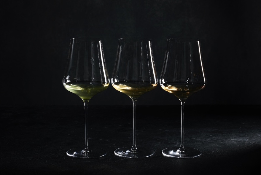 A dark image of three wine glasses lined up in a row against a black background. 