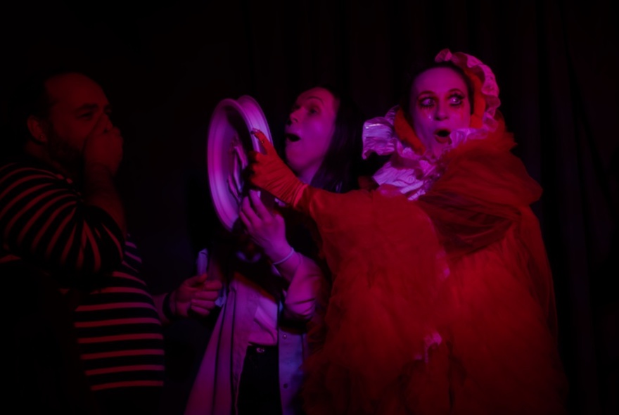 A performer in a dimly lit theatre space interacting with audience members.