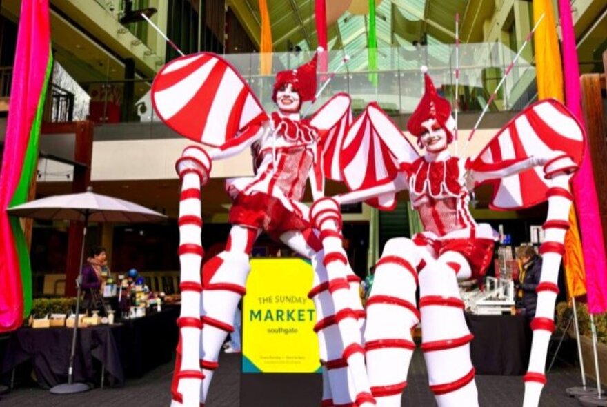 Christmas elf performers on stilts wearing red and white striped outfits.