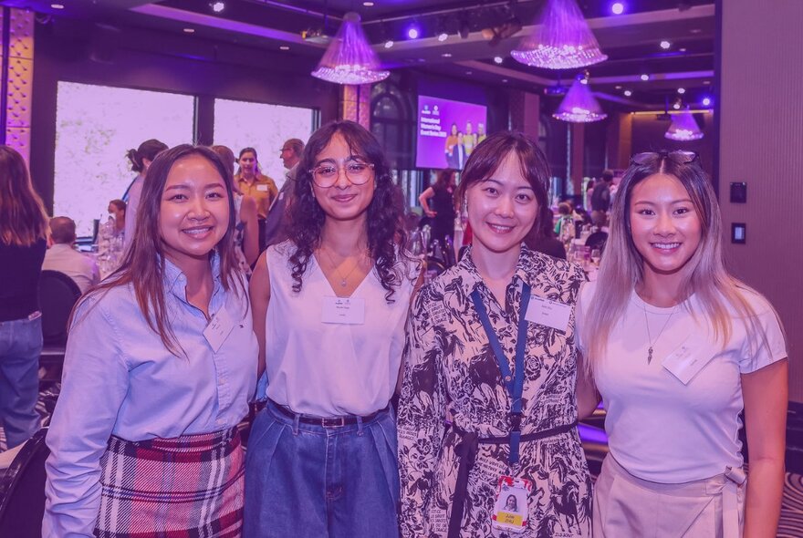 Four women posing for a photo at an indoor event.