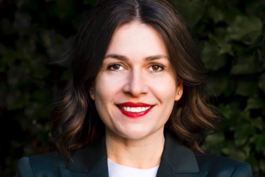 Smiling woman with red lipstick, black jacket and white top.