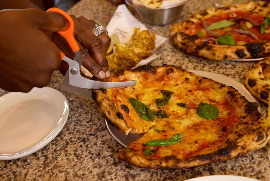 Scissors used to slice up a pizza at a table.