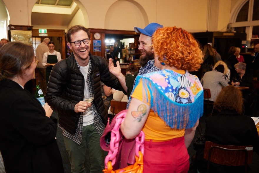 A group of people mingling in a old building, one man laughing.