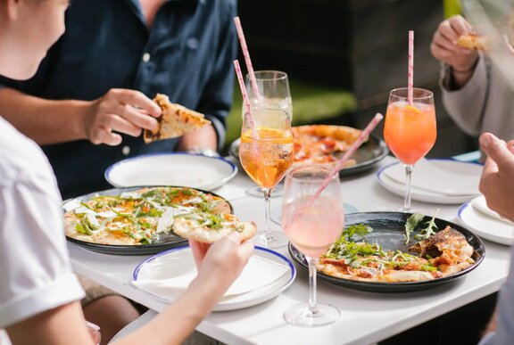 Four people at a table eating pizza, with glasses of spritz in front of them.