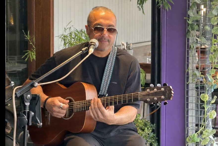 Musician seated at a microphone playing a guitar.