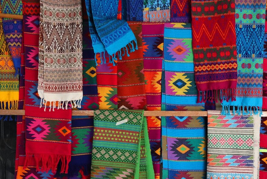 Rows of colourful scarves hanging on wooden hangers featuring traditional folk weaves.