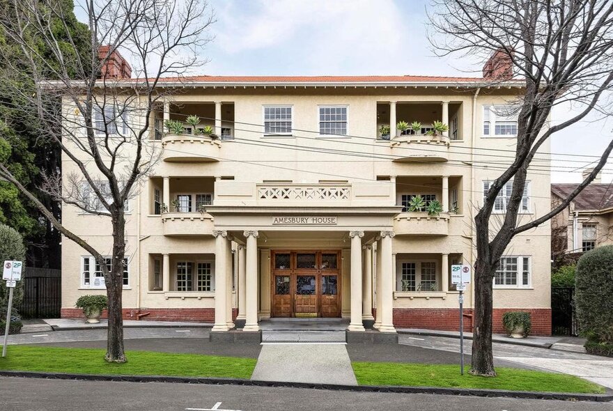 Grand mansion apartment building with portico and trees.