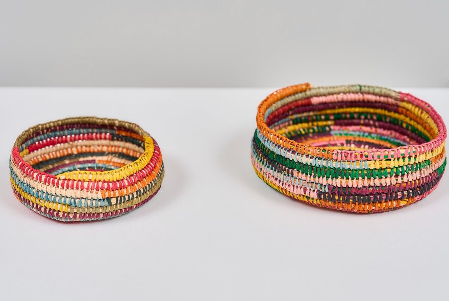Colourful shallow woven baskets on display in the white gallery space at Craft Victoria.