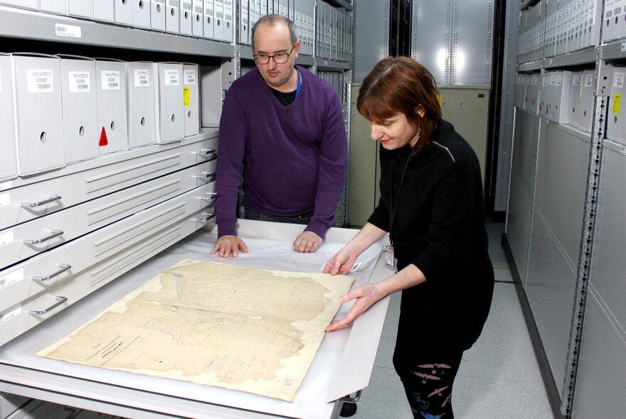 Two archivists looking at a map that is stored in a large pull out drawer at the Victoria State Archives.