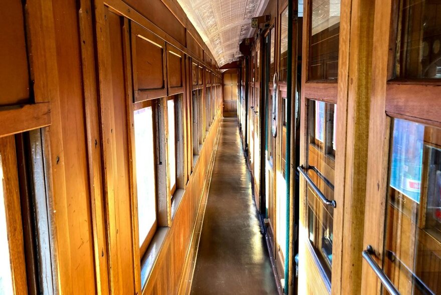 Vintage train corridor with wooden panelling and sliding windows.