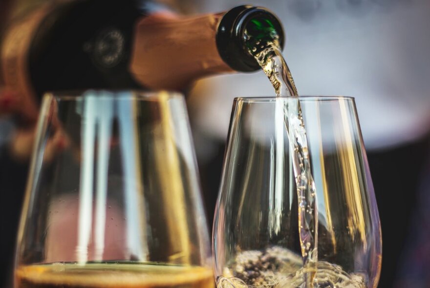 Sparkling wine being poured from a bottle into two glasses.