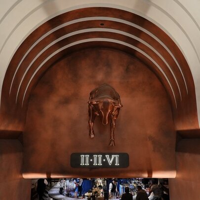An underground archway entrance to a basement restaurant with a copper-toned background featuring a bull sculpture and the Roman numerals II-II-VI.