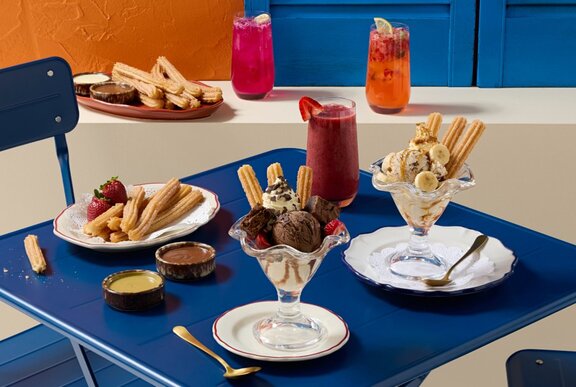 A blue table and chair set with ice cream sundaes and fruity drinks. 