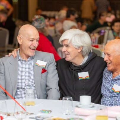 A group of older adults smiling and interacting at a table during a community gathering.