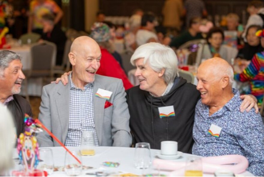 A group of older adults smiling and interacting at a table during a community gathering.