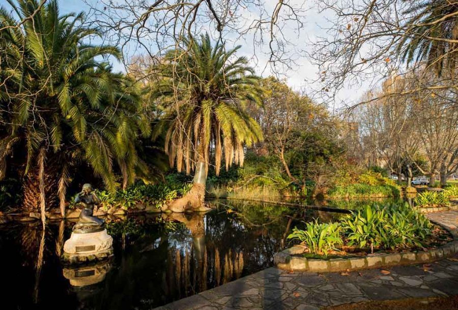 A pond surrounded by trees and pavers with a statue in the centre.