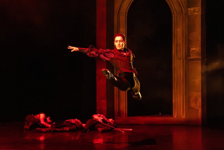 A gothic Dracula figure standing on a stage, his arm outstretched above a body on the floor.