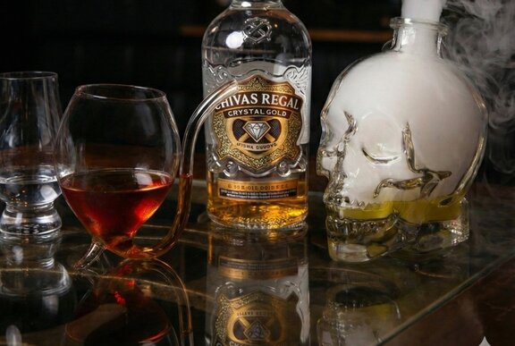 A bottle of whisky next uniquely shaped glass with a curved stem from the bottom that functions as a straw.