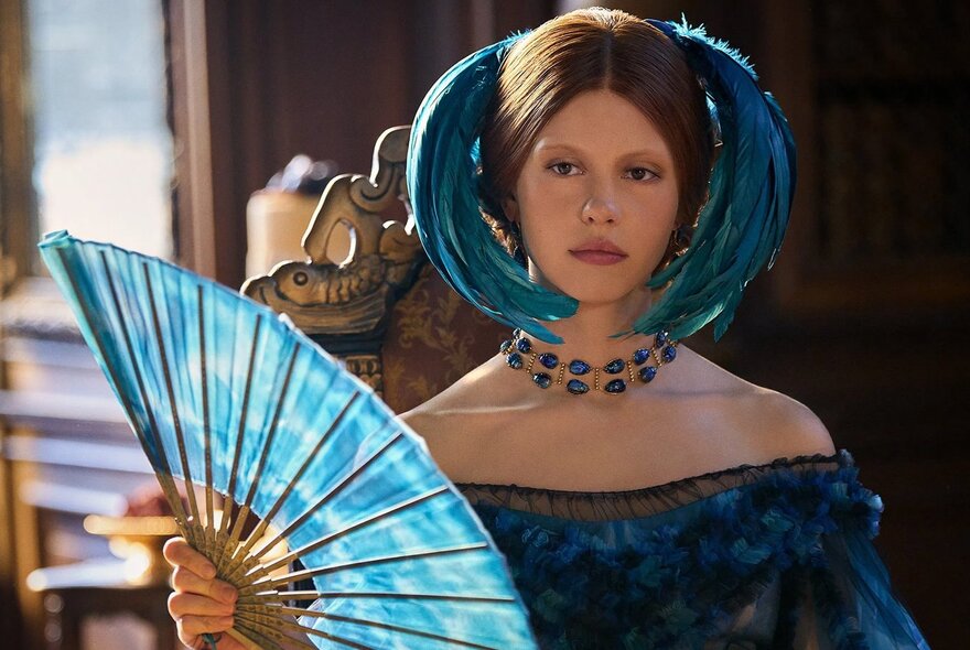 Woman with blue headress holding a blue fan.