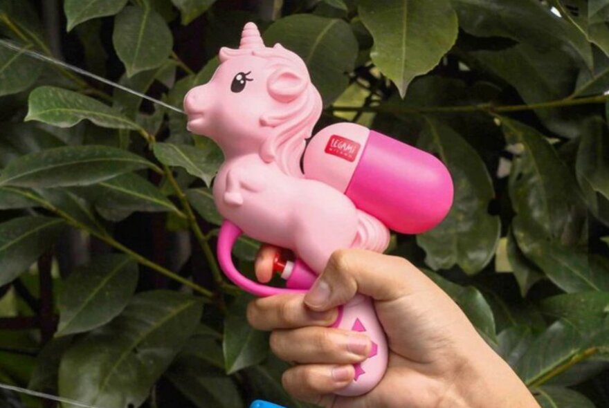 A person is shooting a water gun in the shape of a pink unicorn.