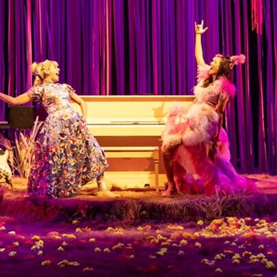 Two actors performing on a stage with purple curtains and a piano.