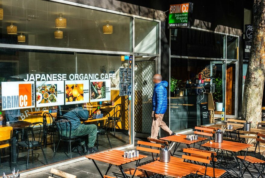 A man walking into a cafe with outdoor seating.