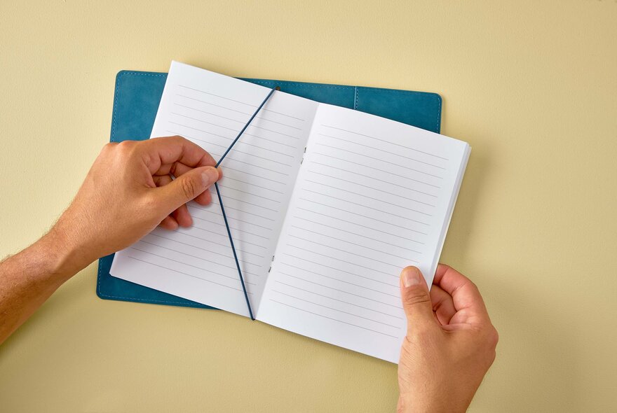 Hands holding a blue journal with cover and strap.