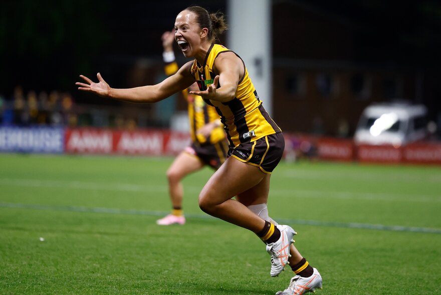 A Hawthorn Hawks AFLW player with her arms spread wide in celebration during a game.