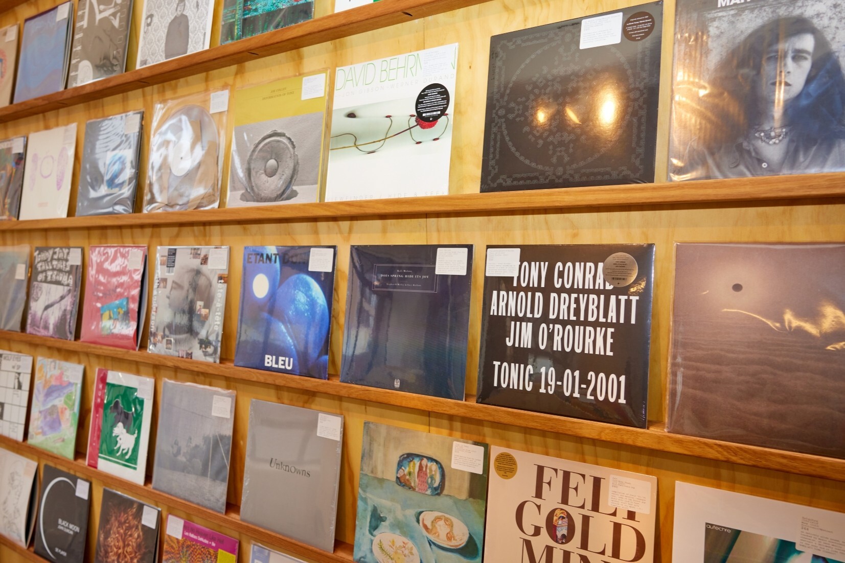 A wall of colourful vinyl records on a wooden shelf