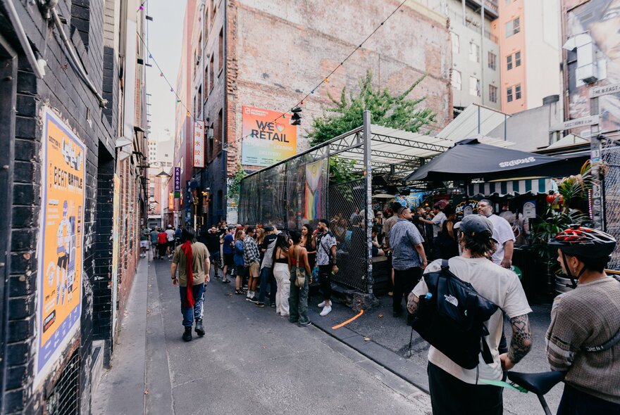 People mingling outside in the laneway around Section 8, an iconic open-air bar and music venue, surrounded by high rise city buildings.