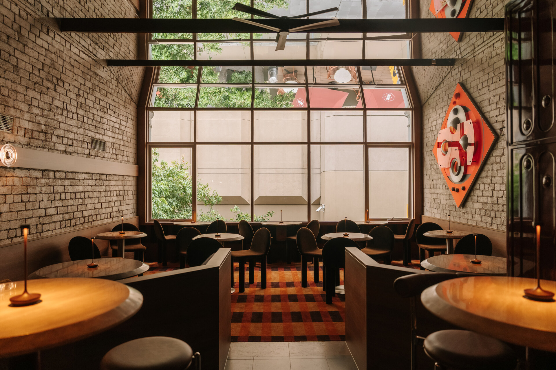 The interior of a restaurant with a roof height window, brick walls and dark wooden tables and chairs