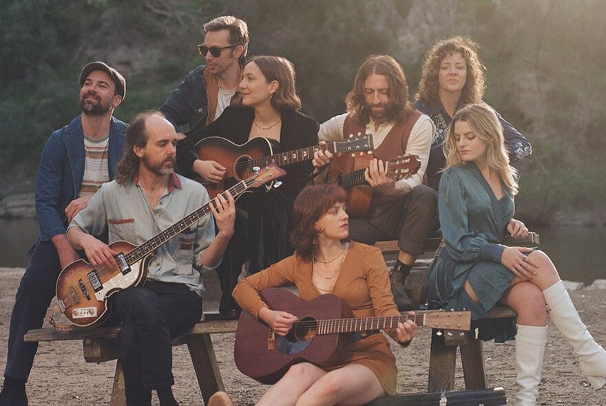 A collection of musicians, some with guitars, posing in 1960s folk music style clothing. 