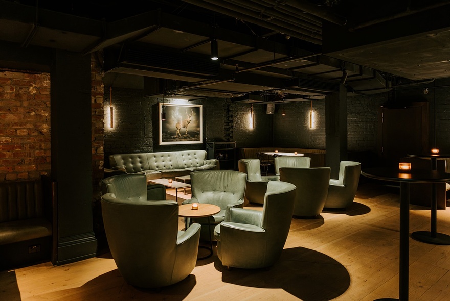 Armchairs around table in a dimly-lit black cocktail bar.