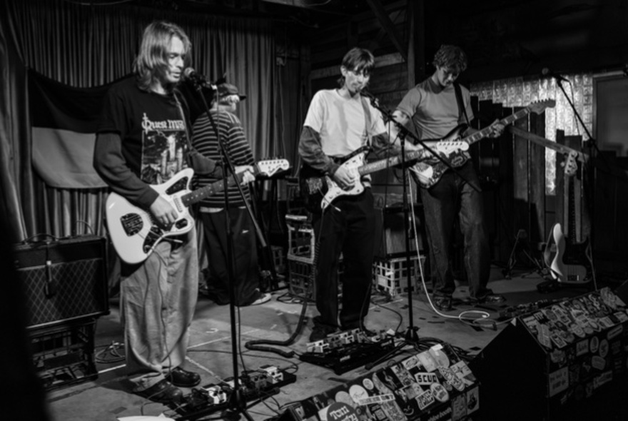 A black and white photograph of a three-guitarist band on stage.