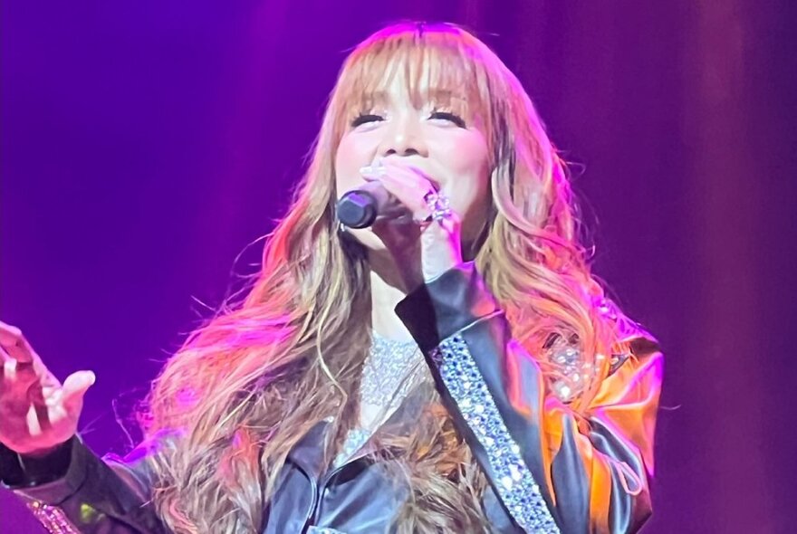 Filipino singer Nina wearing black leather with rhinestones singing live with a microphone under pink lights.