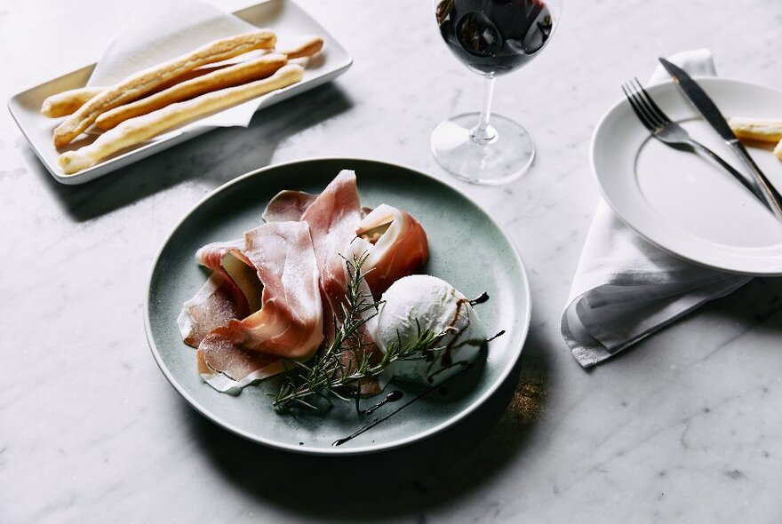 A plate of cold meats and soft cheese, with a glass of wine on a restaurant dining table.