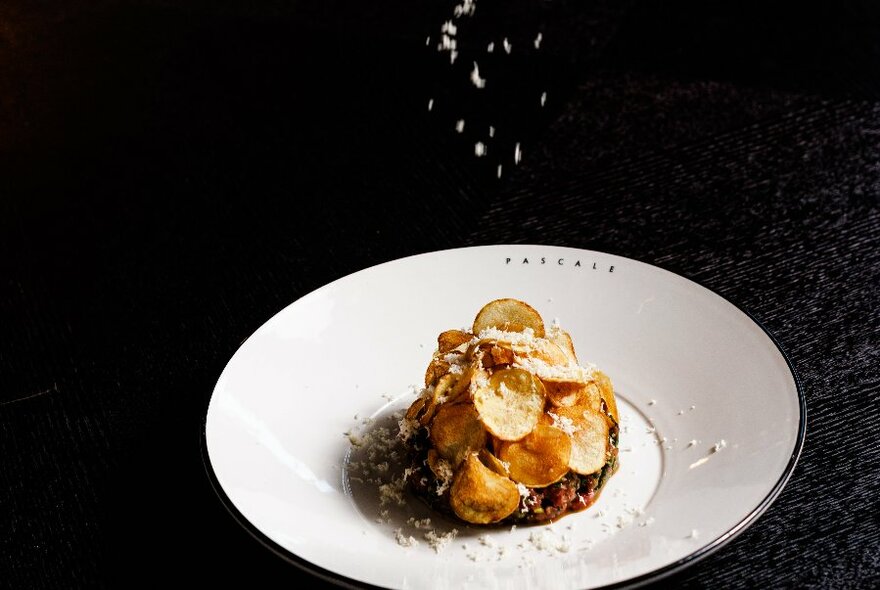 Parmesan dropping onto a white dish of food against a dramatic black background.