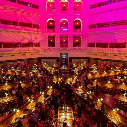 The Dome reading room of State Library Victoria showing the upper level balconies, and rows of desk fanning out from the centre, all bathed in a pink light.