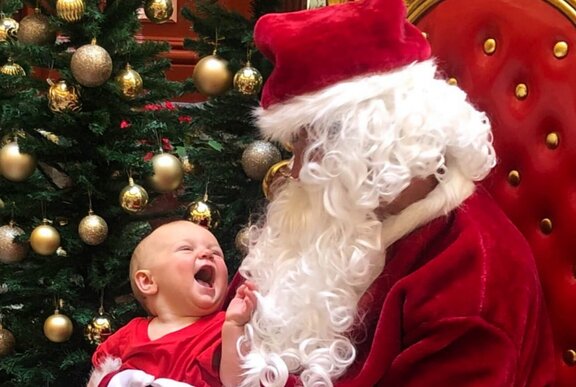 A smiling baby sitting on Santa's lap. 