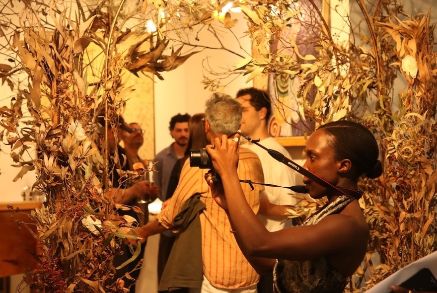 People looking at and photographing foliage and artworks in a gallery space.