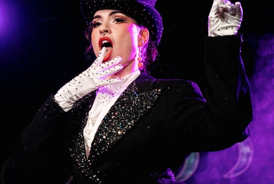 A burlesque dancer in a top hat, white gloves and sequin studded jacket.
