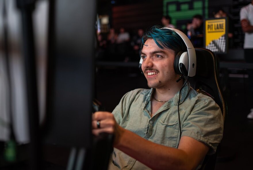 Person seated in a F1 Grand Prix game car, holding the steering wheel and wearing headphones.