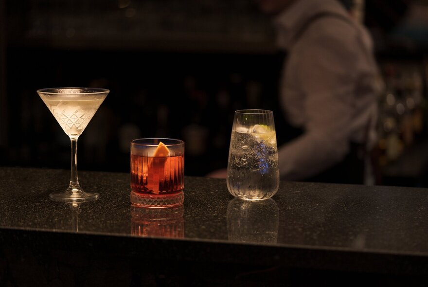 Backlit cocktails glowing on a darkly lit bar.