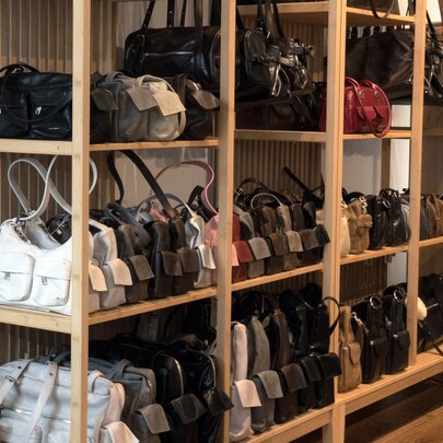 Rows of colour-coded leather handbags displayed on a wooden shelf in a shop.