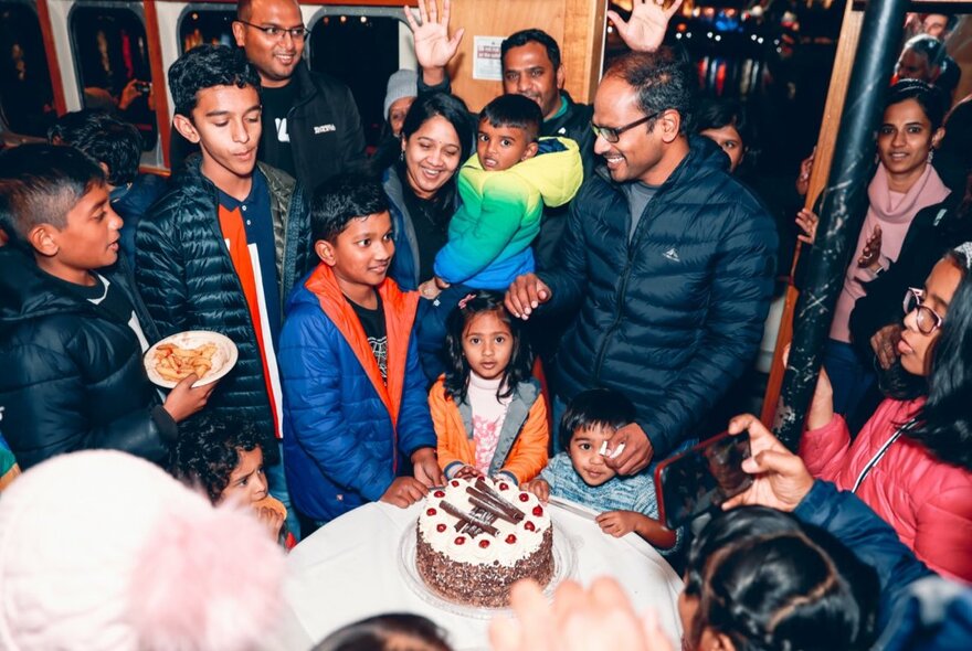 A group of warmly dressed people celebrating a birthday for a child with a birthday cake.