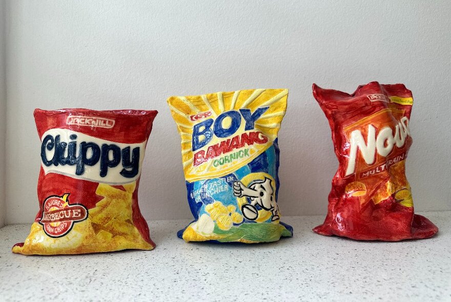 Artwork of three coloured snack food packets on a white surface.