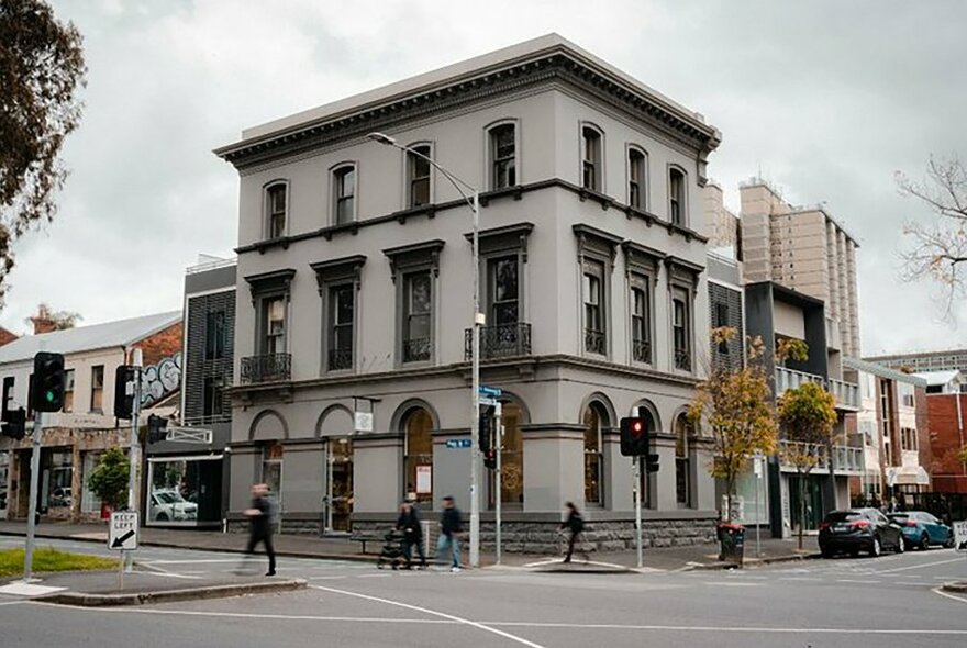 Three storey, white, Victorian-era building, on a corner, against cloudy sky backdrop. 