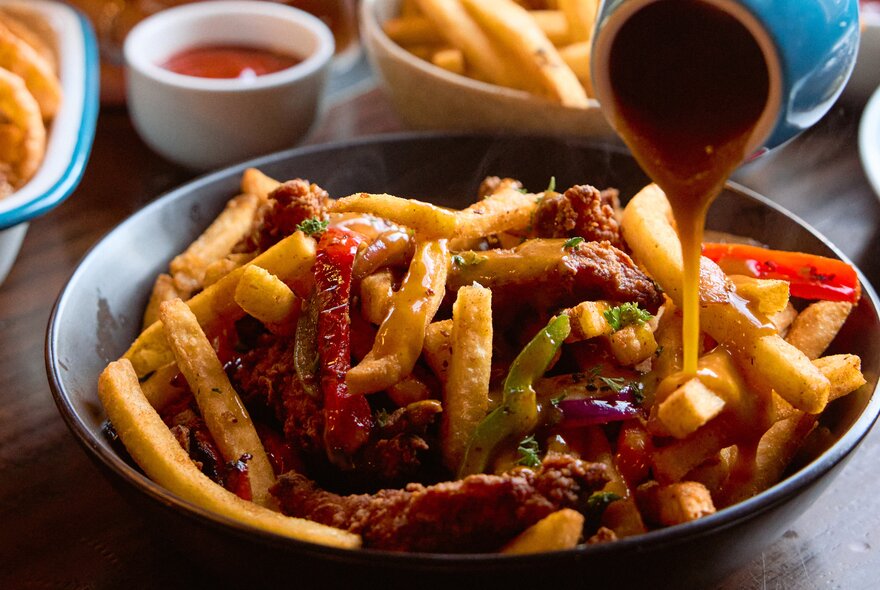 An Irish spice bag with chips, chicken fingers, vegetables and gravy.